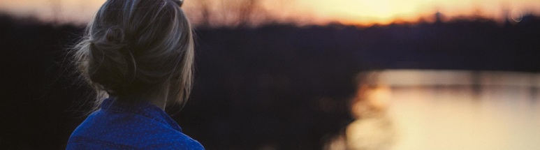 Frau von hinten schaut auf einen See bei Sonnenuntergang